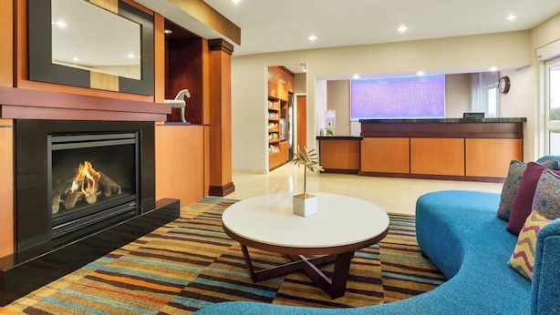 Een moderne hotellobby met een open haard, een ronde salontafel, een blauwe bank en een receptiebalie.