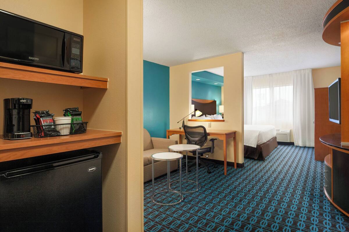 Een hotelkamer met een kitchenette, een bed, een bureau en een zithoek.