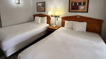 A hotel room with two single beds, a nightstand with a telephone, and two wall-mounted lamps.