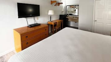 A hotel room with a bed, wooden dresser, desk, chair, television, and a bathroom with a mirror and sink.