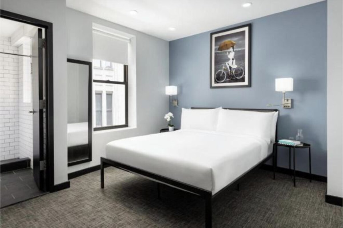 A hotel room with a large bed, a nightstand, a lamp, and a framed picture on the wall.