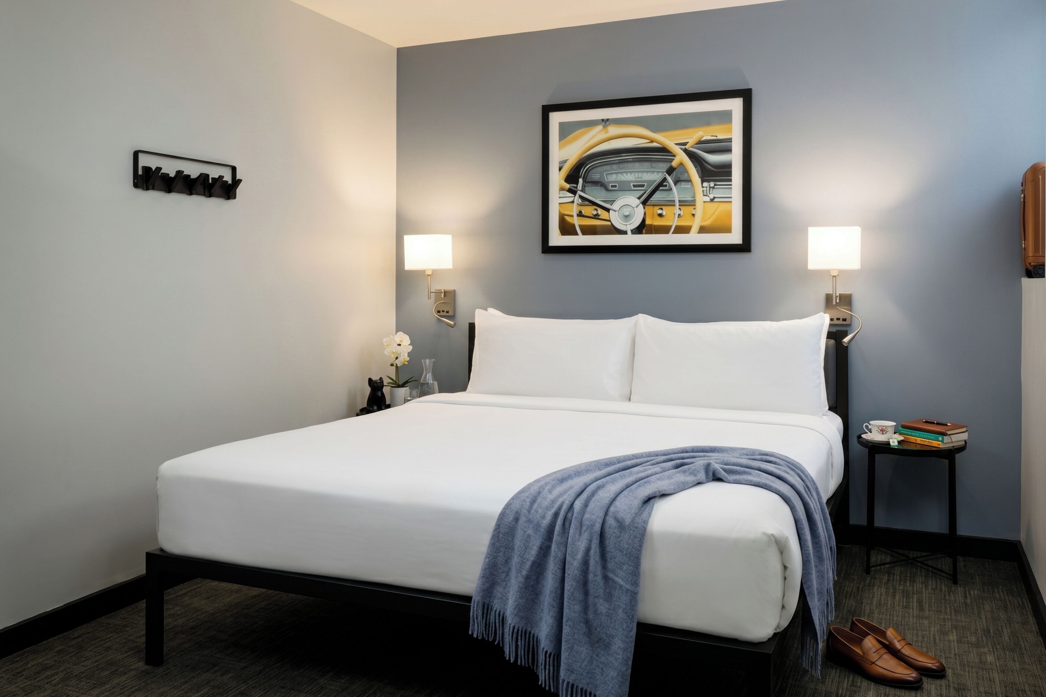 A neatly made bed with a white comforter, a blue throw blanket, and a pair of shoes on the floor.