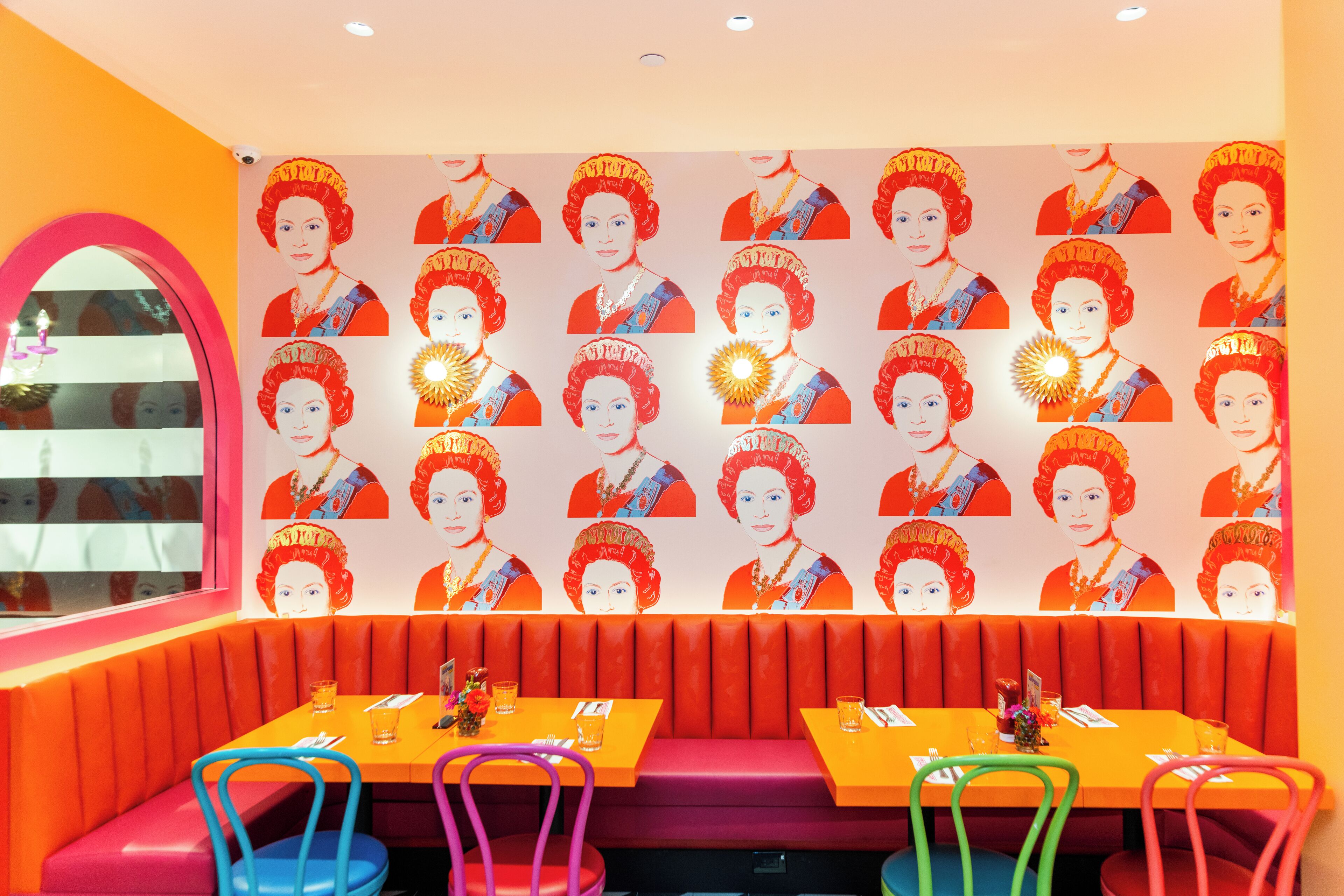 Un restaurante con paredes de color naranja intenso, un mural decorado y asientos coloridos.