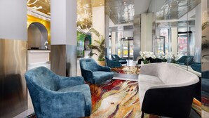A modern lobby with blue armchairs, a white sofa, and a colorful abstract carpet. - OYO Times Square (New York)