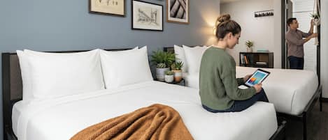 Een hotelkamer met een bed, een nachtkastje met een plant en een wand met ingelijste botanische illustraties.