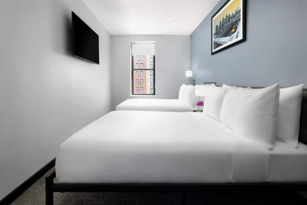 A hotel room with a large bed, a flat-screen TV mounted on the wall, and a window with a cityscape view.