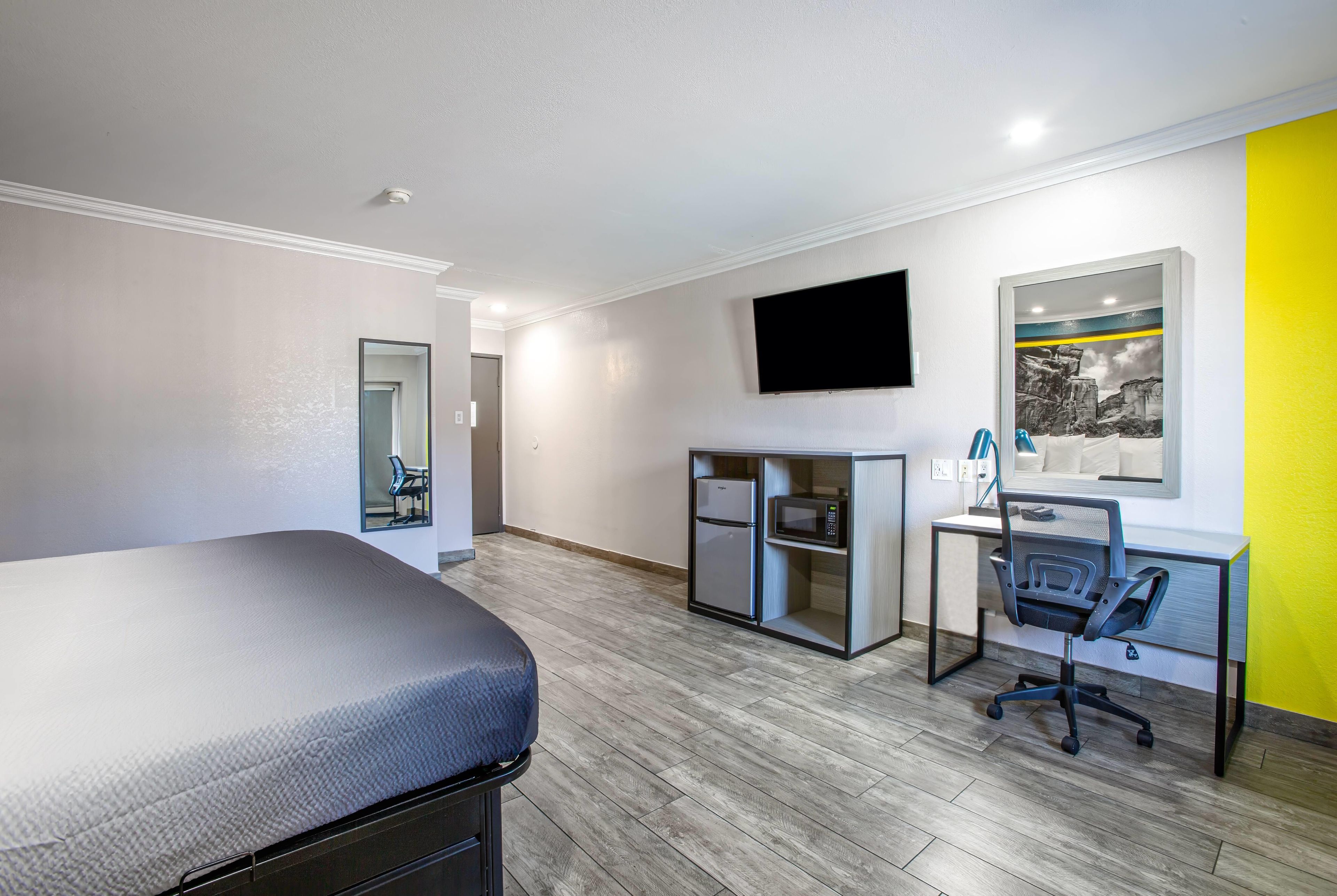 Une chambre d’hôtel équipée d’un lit, d’un bureau avec une chaise, d’un four à micro-ondes et d’un téléviseur à écran plat fixé au mur.