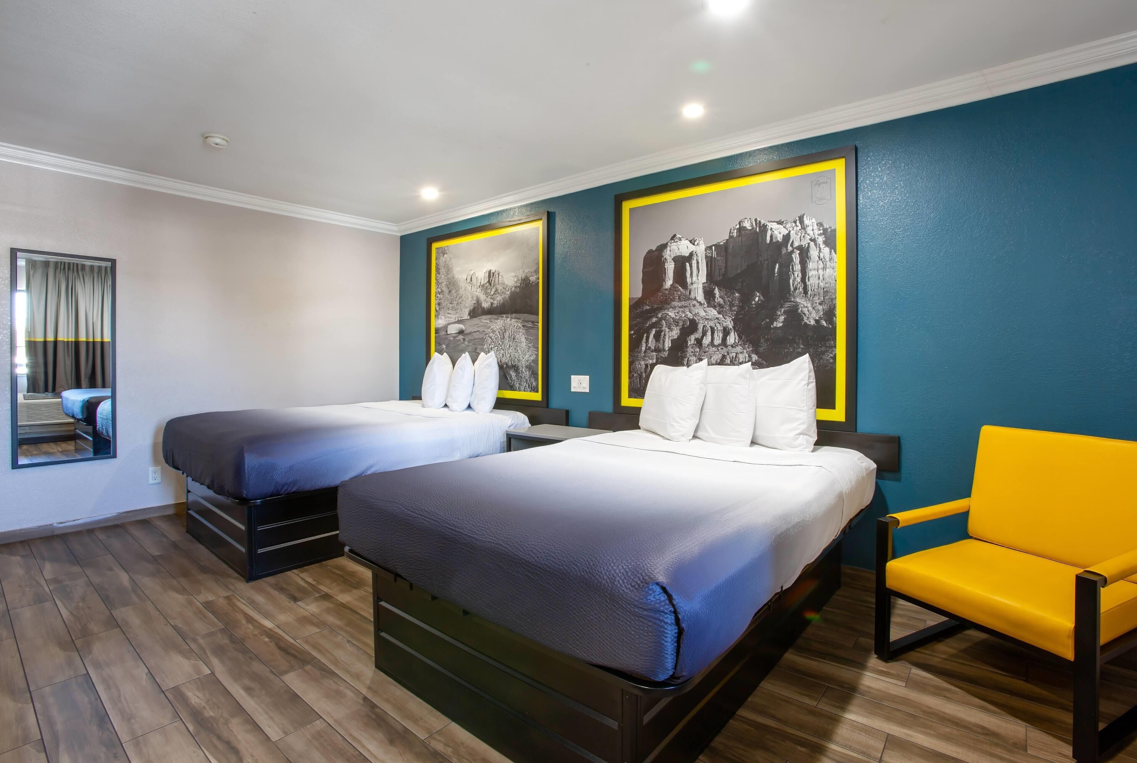 Quarto de hotel com duas camas, um espelho, uma cadeira amarela e duas fotografias grandes a preto e branco nas paredes.