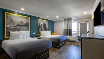 Quarto de hotel com duas camas, uma escrivaninha, uma cadeira e uma janela grande.