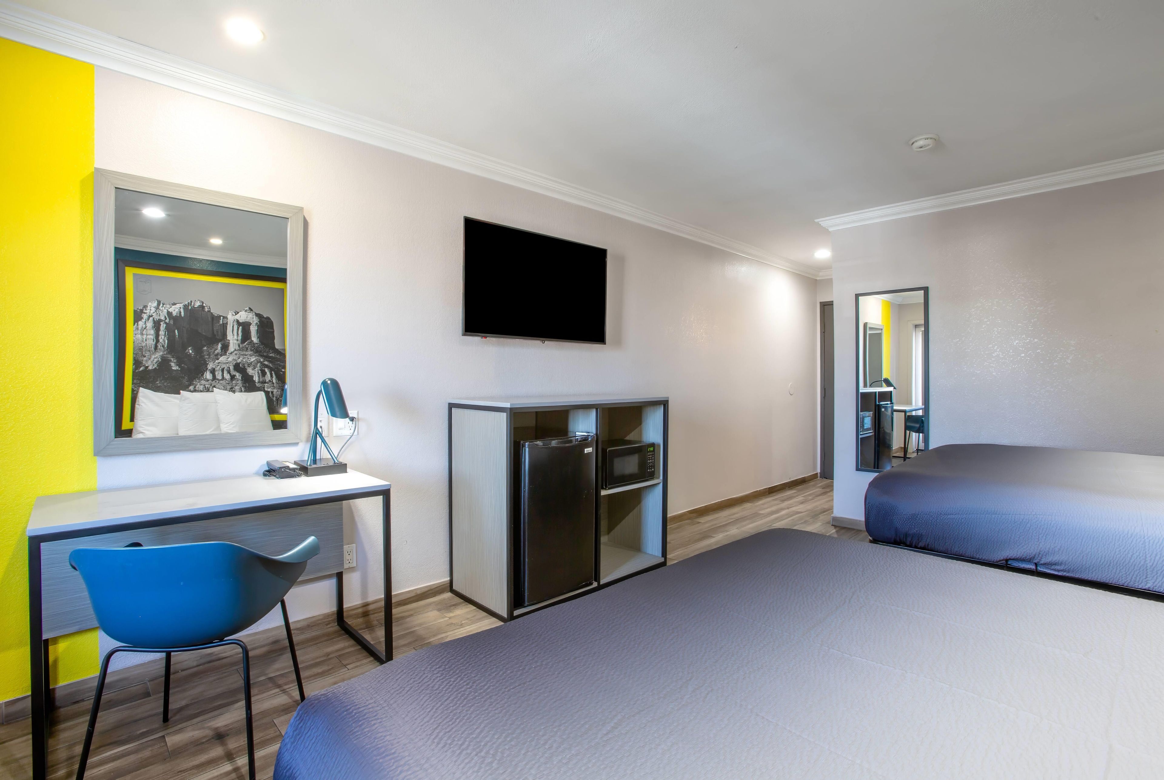 A hotel room with a desk, a chair, a bed, a television, and a microwave.
