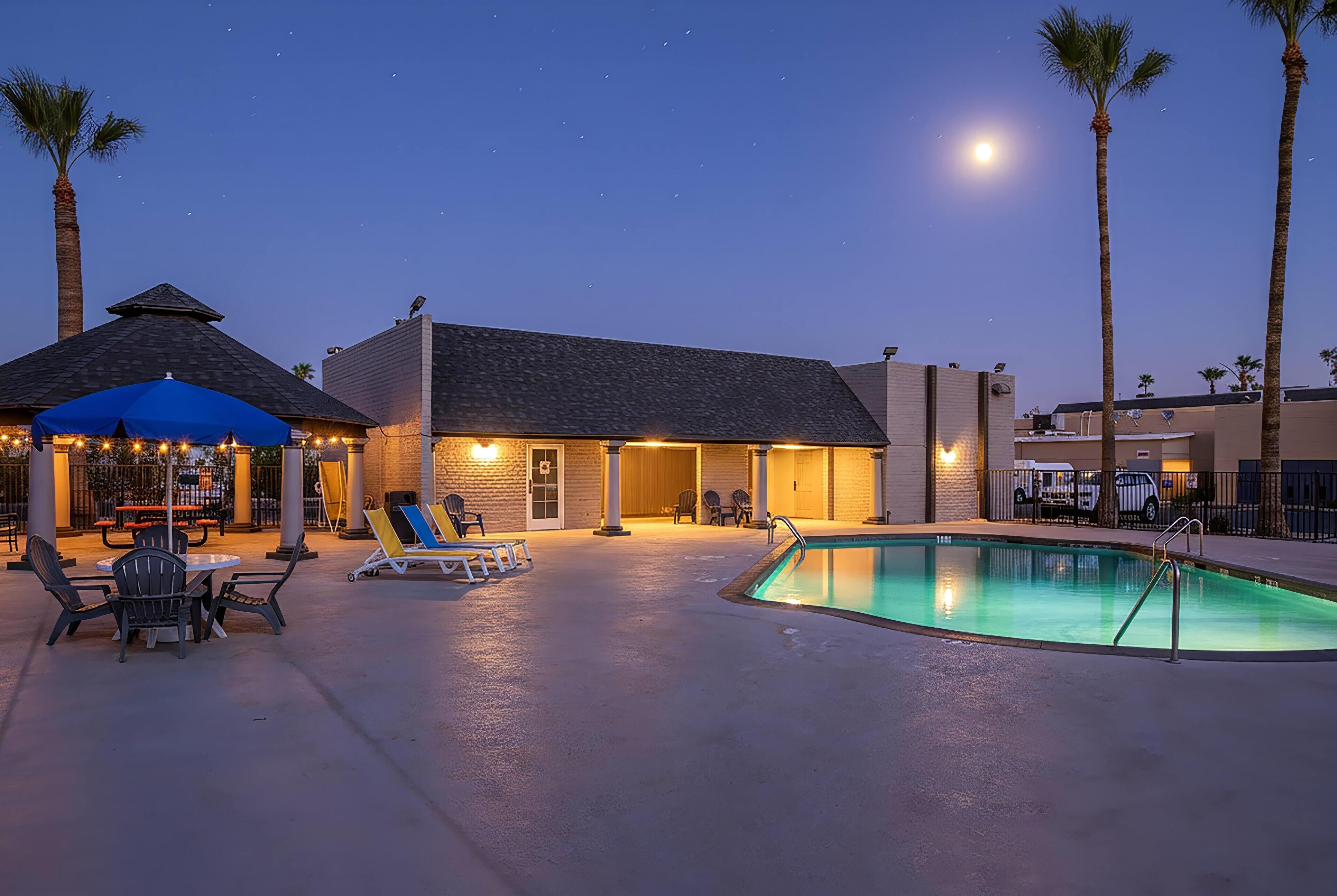 A pool area with lounge chairs, a bar, and a building with a sloped roof.