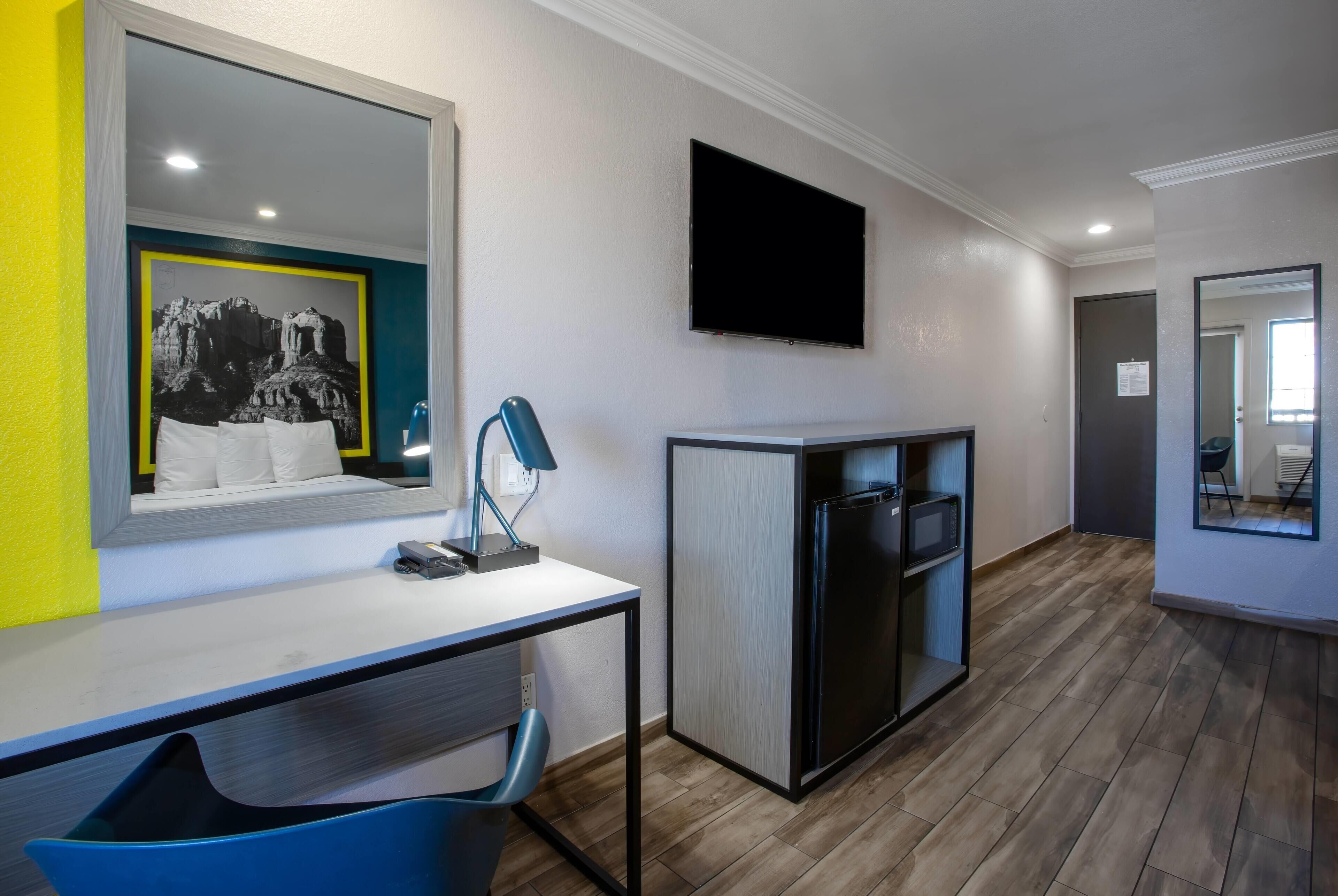 Une chambre d’hôtel moderne équipée d’un bureau, d’une chaise, d’un téléviseur à écran plat et d’un réfrigérateur.