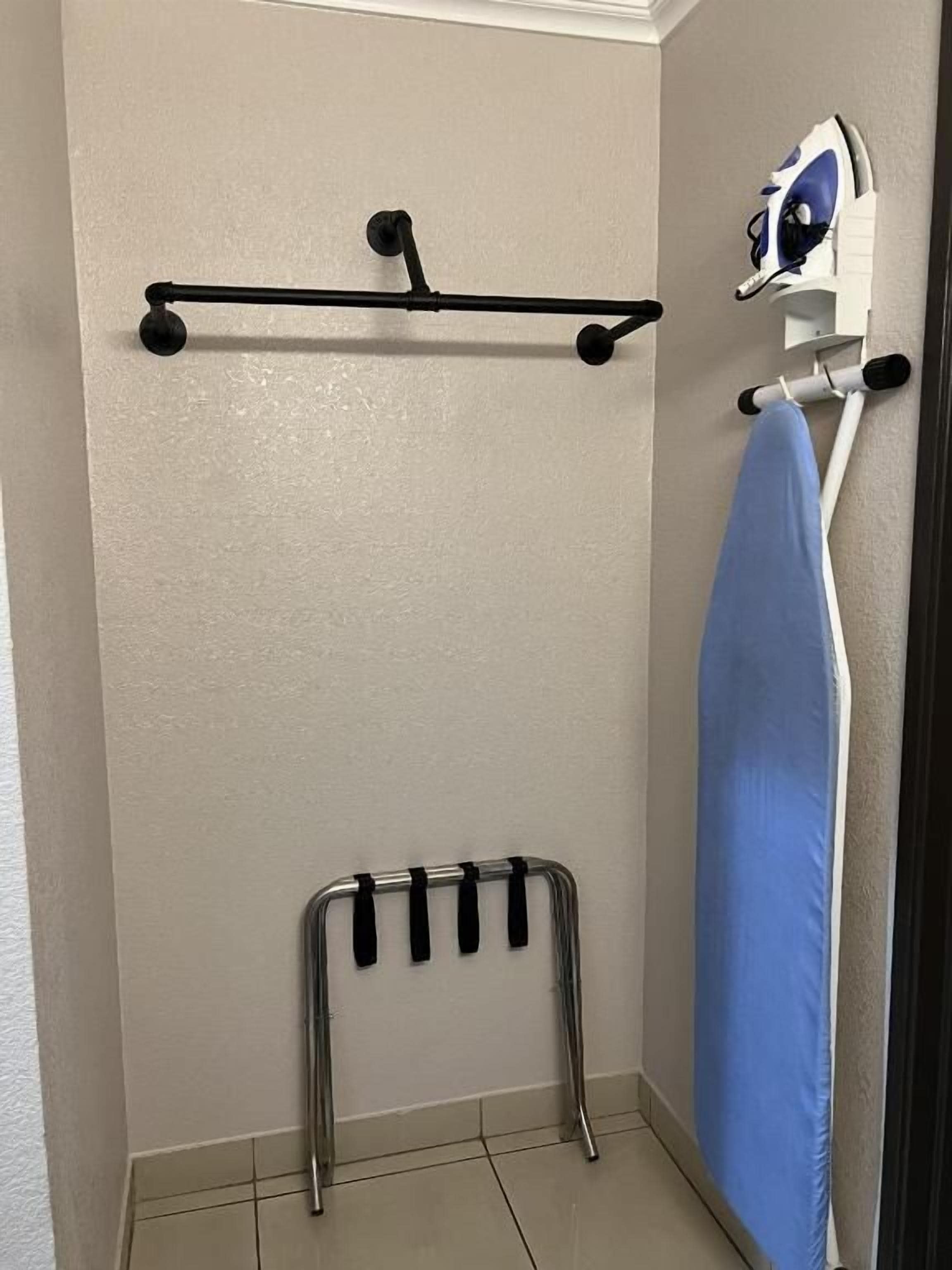 Un baño con toallero, tabla de planchar y cortina de ducha.