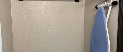 A bathroom with a towel rack, an ironing board, and a shower curtain.