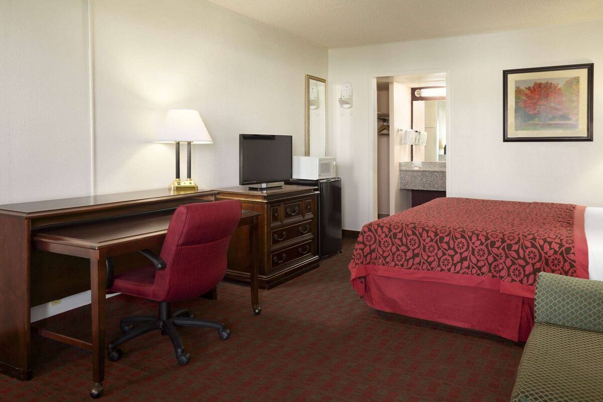 Habitación de hotel con escritorio, silla, televisor, cómoda y cama con colcha estampada.