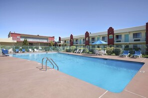 A swimming pool with lounge chairs and a building with multiple balconies in the background.