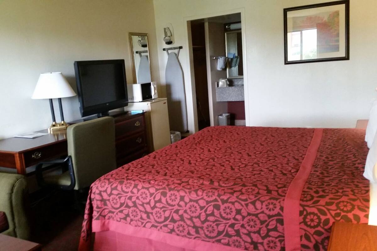 Habitación de hotel con cama, escritorio con televisor, una silla, lámpara de escritorio y espejo.