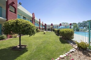 A well-maintained courtyard with a swimming pool, a neatly trimmed lawn, and a row of buildings with balconies.