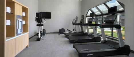 A gym with treadmills, a water dispenser, and a TV on a stand.