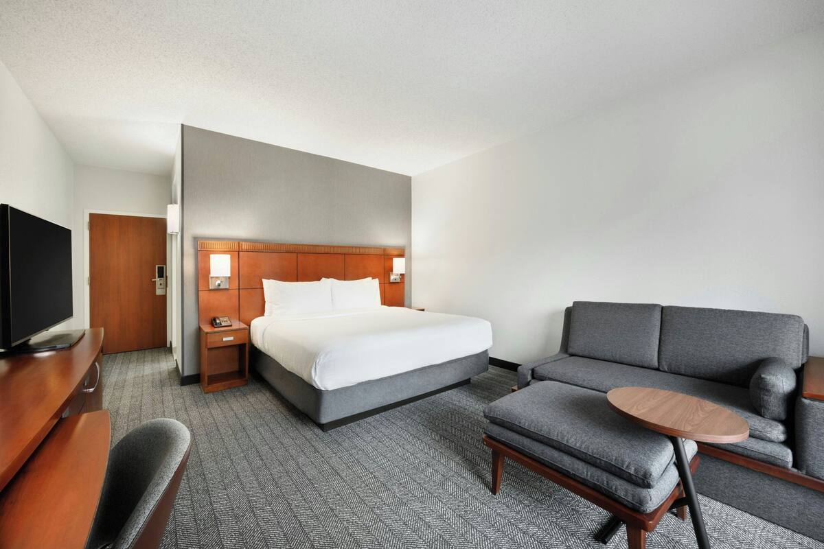 A hotel room with a bed, a sofa, a small table, a TV, and a desk.