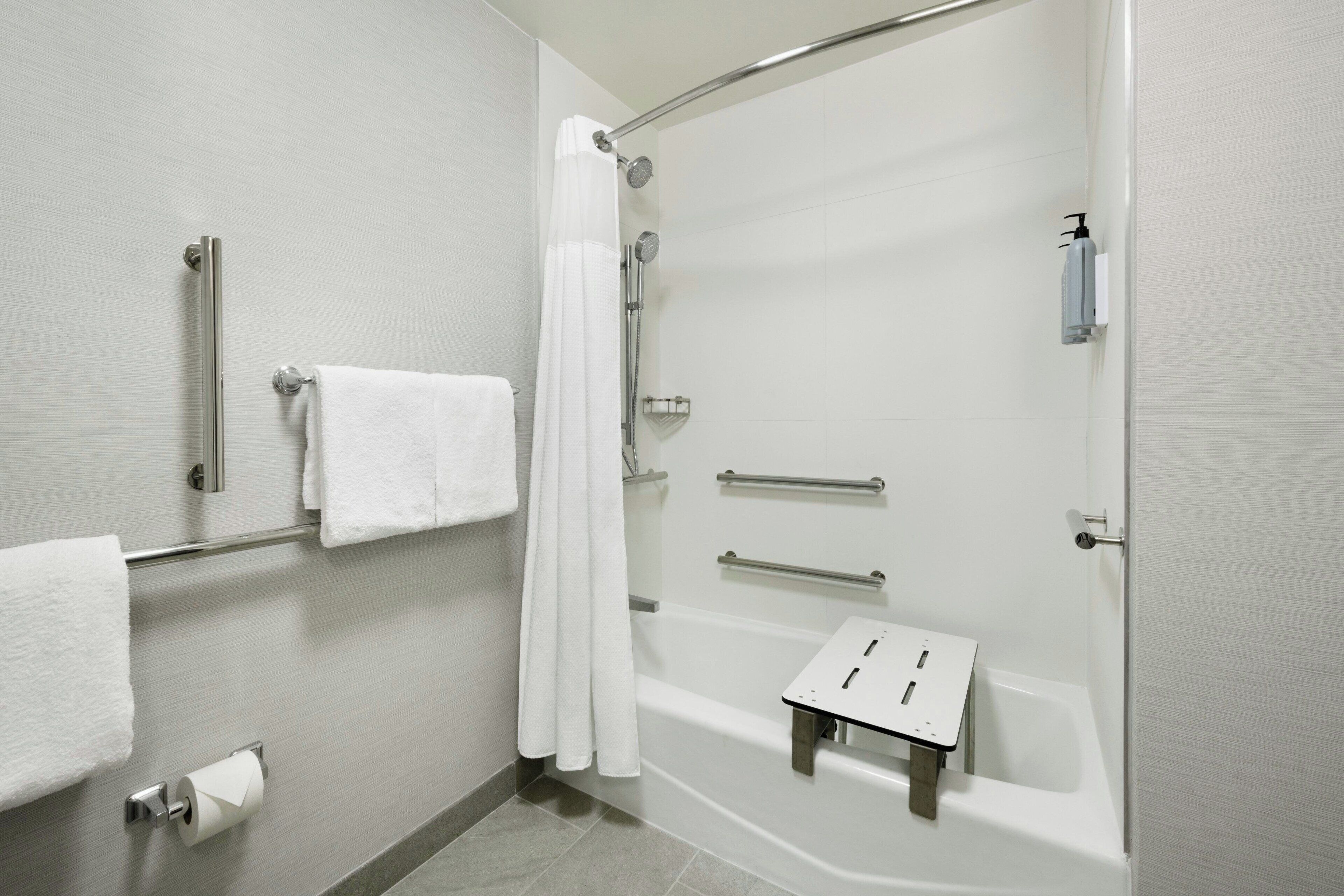 Une salle de bain moderne dotée d’une douche à l’italienne, de barres d’appui, d’un porte-serviettes et d’un support à papier toilette.