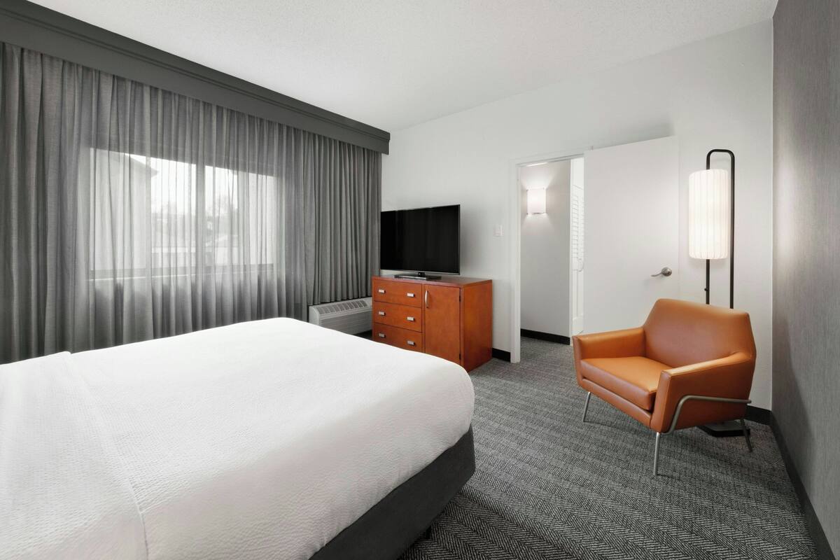 A hotel room with a bed, a TV, a dresser, a chair, and a lamp.