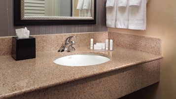 A bathroom with a granite countertop, a sink, a mirror, and a towel rack with white towels.