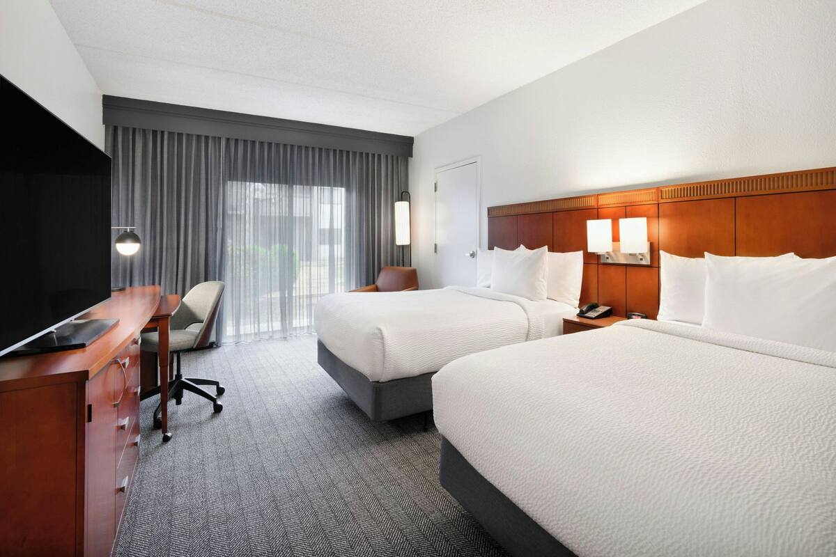 A hotel room with two beds, a desk, a chair, and a television.