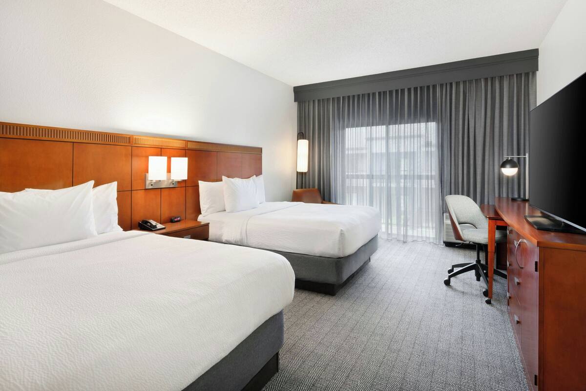 A hotel room with two beds, a desk, a chair, and a TV.