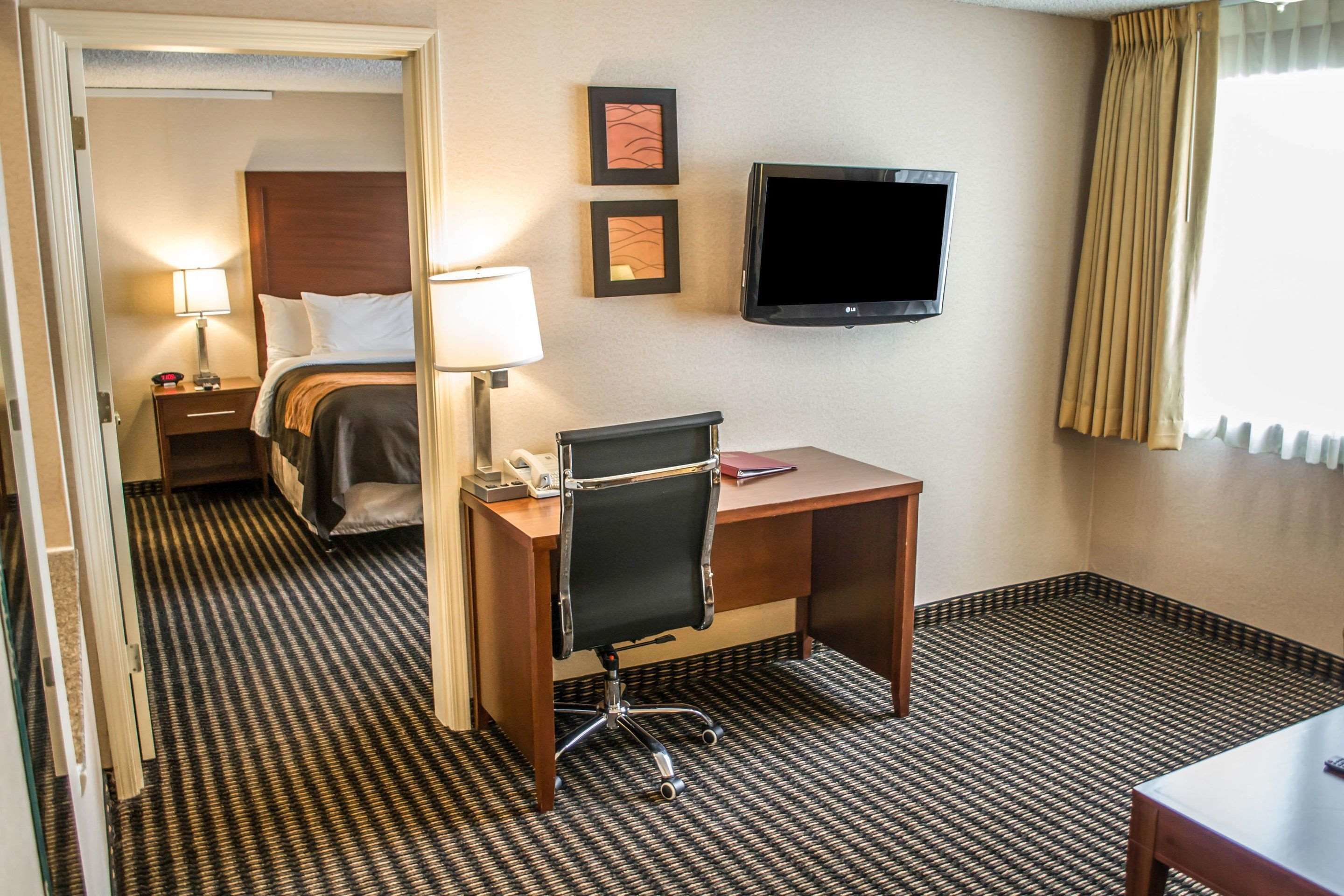 A hotel room with a bed, desk, chair, TV, and a door leading to another room.