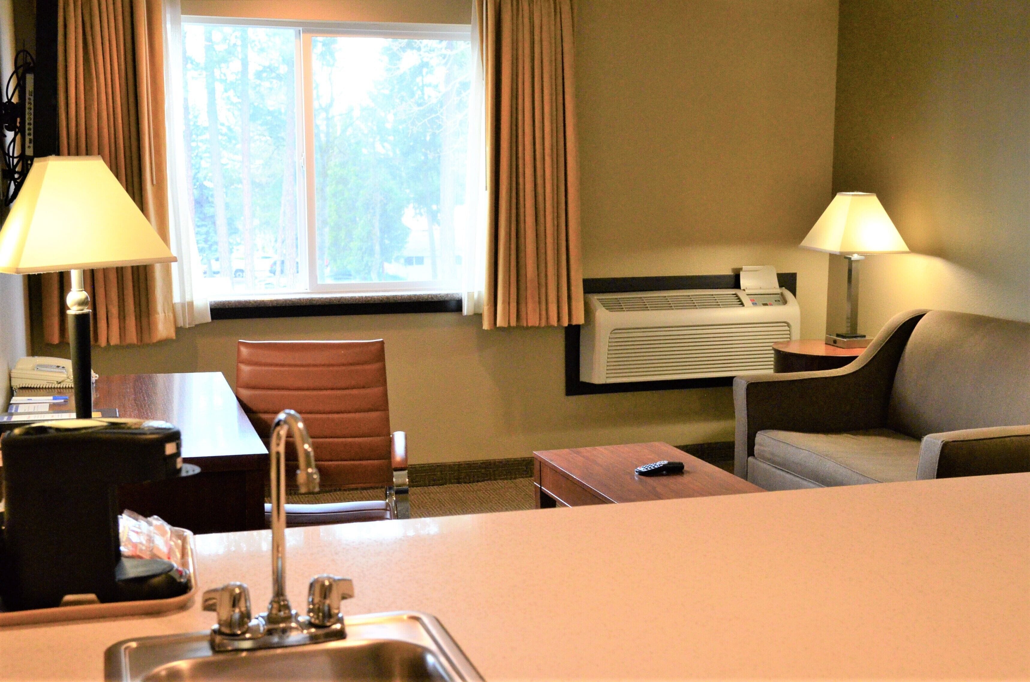 A hotel room with a desk, chair, sofa, and a window with curtains.
