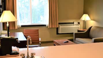 A hotel room with a desk, chair, sofa, and a window with curtains.