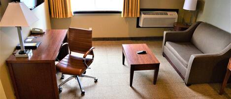 A hotel room with a desk, office chair, sofa, and a small table.