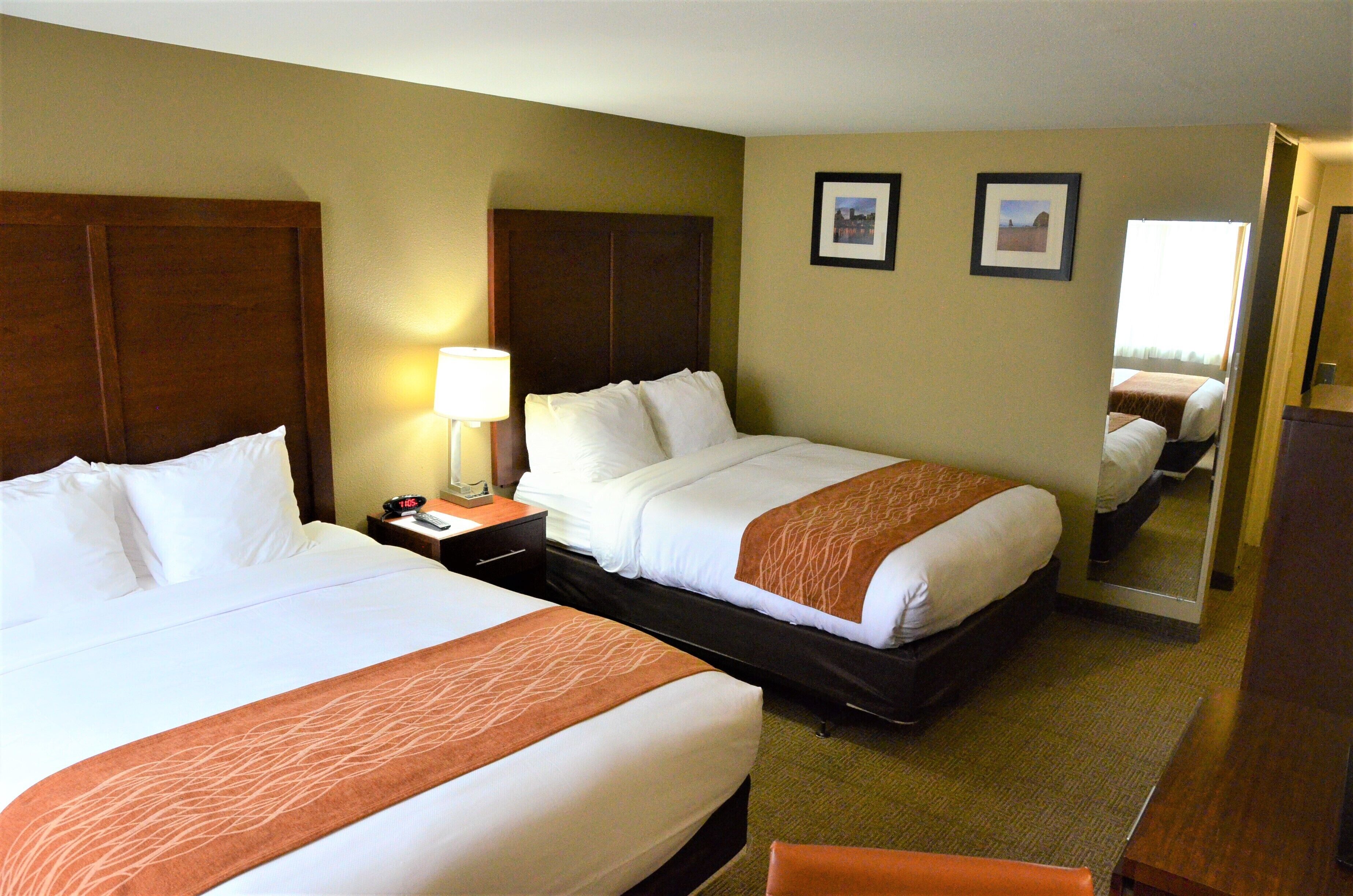 A hotel room with two beds, a nightstand with a lamp, and a mirror on the wall.