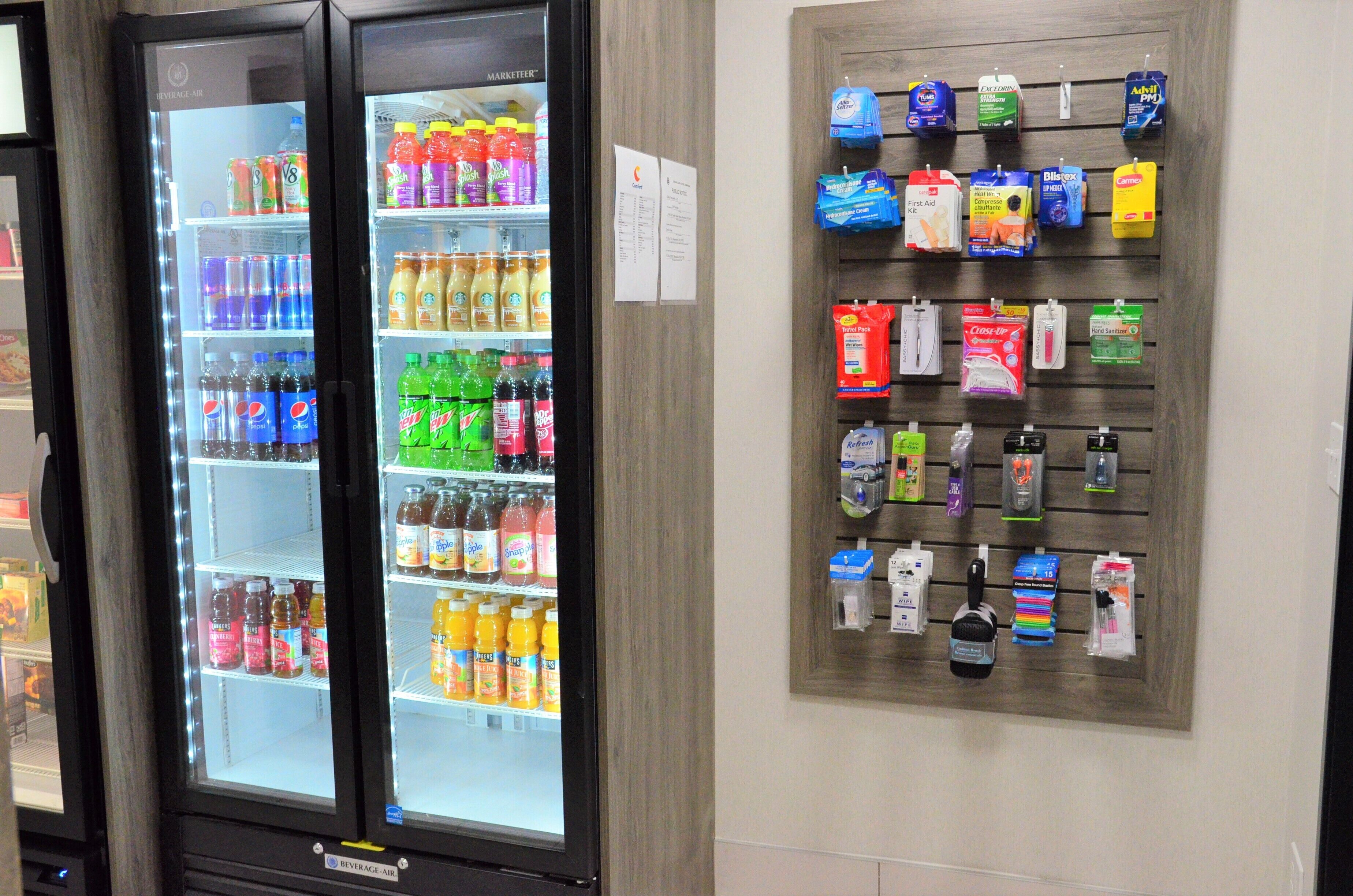 A beverage cooler stocked with various drinks and a wall-mounted display of toiletries and personal care items.