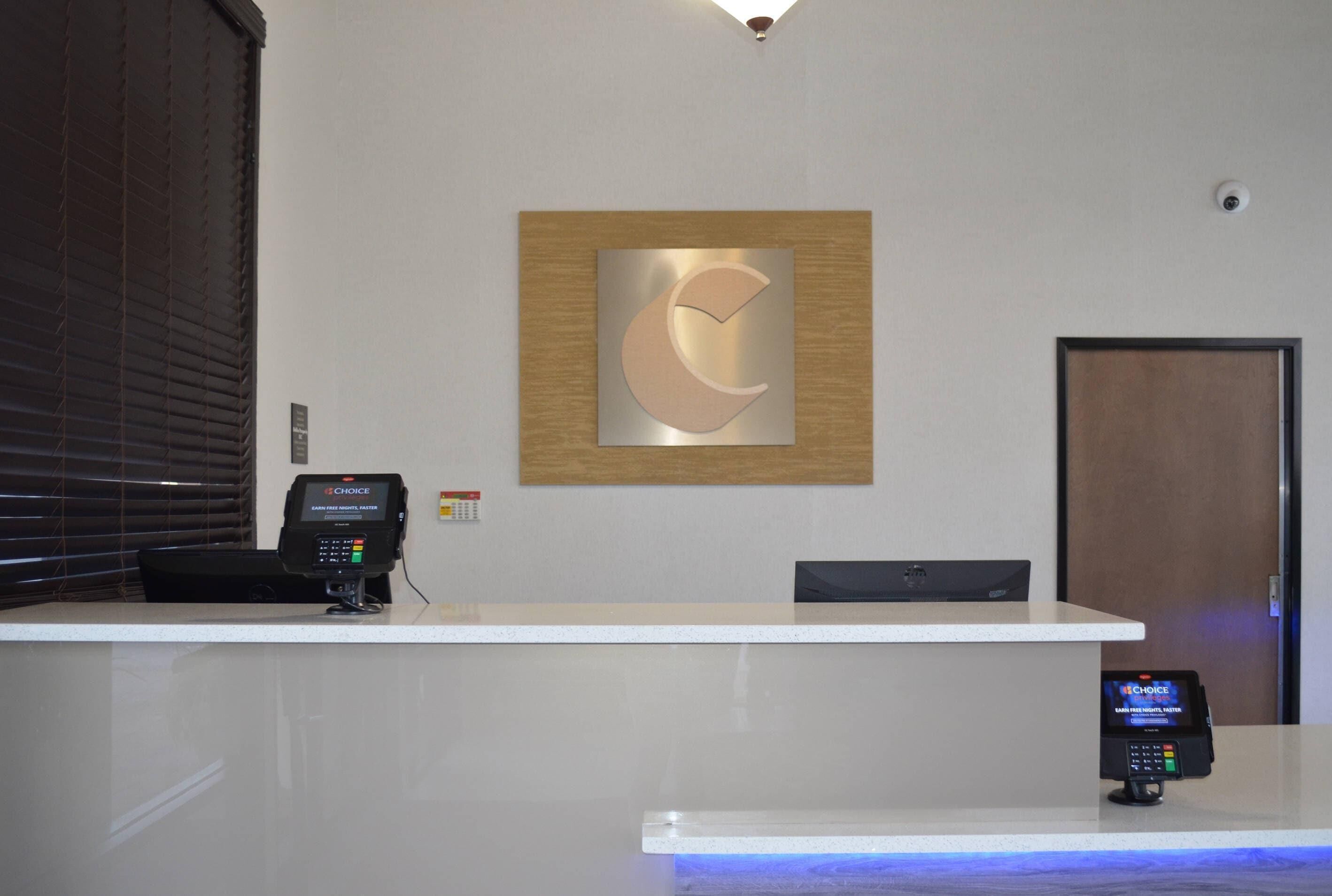 A reception desk with a modern design, including a logo on the wall, a cashless payment terminal, and a security camera.