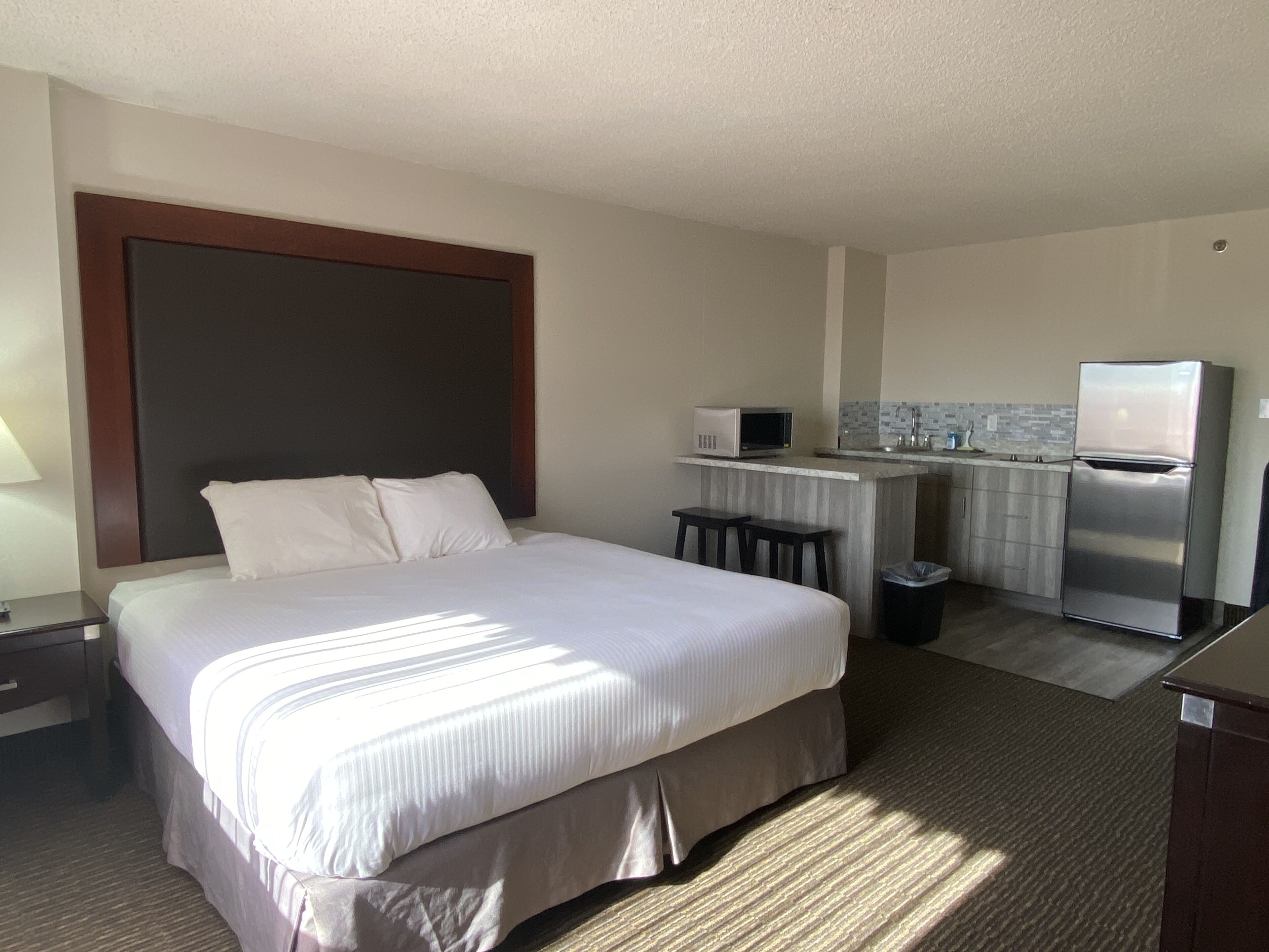A hotel room with a large bed, a small kitchenette, and a desk.