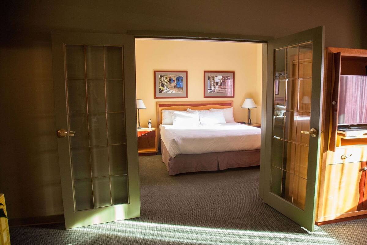 A hotel room with a bed, two bedside lamps, and two framed pictures on the wall.