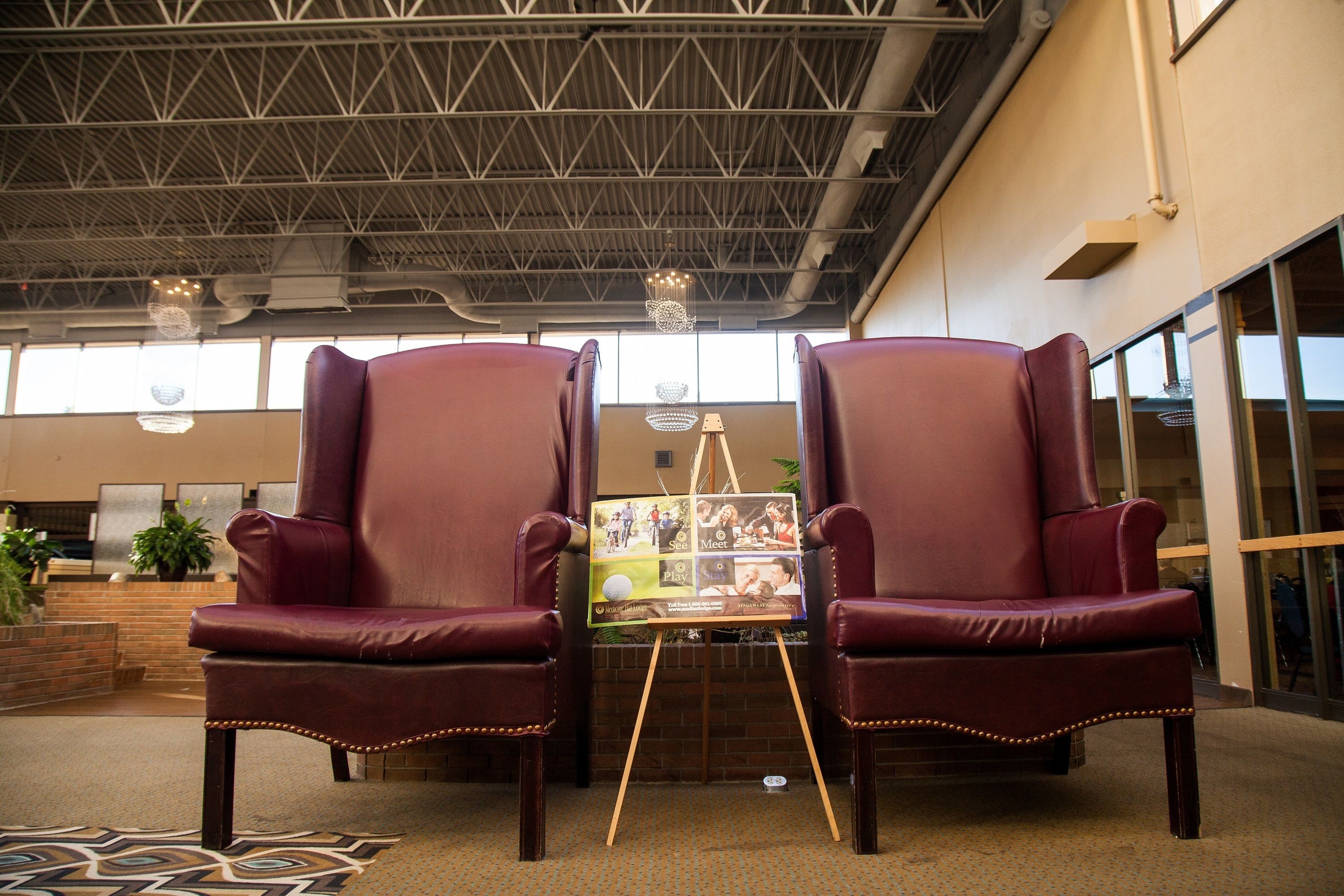 A lobby with two leather armchairs, a wooden easel with a collage, and a patterned carpet.