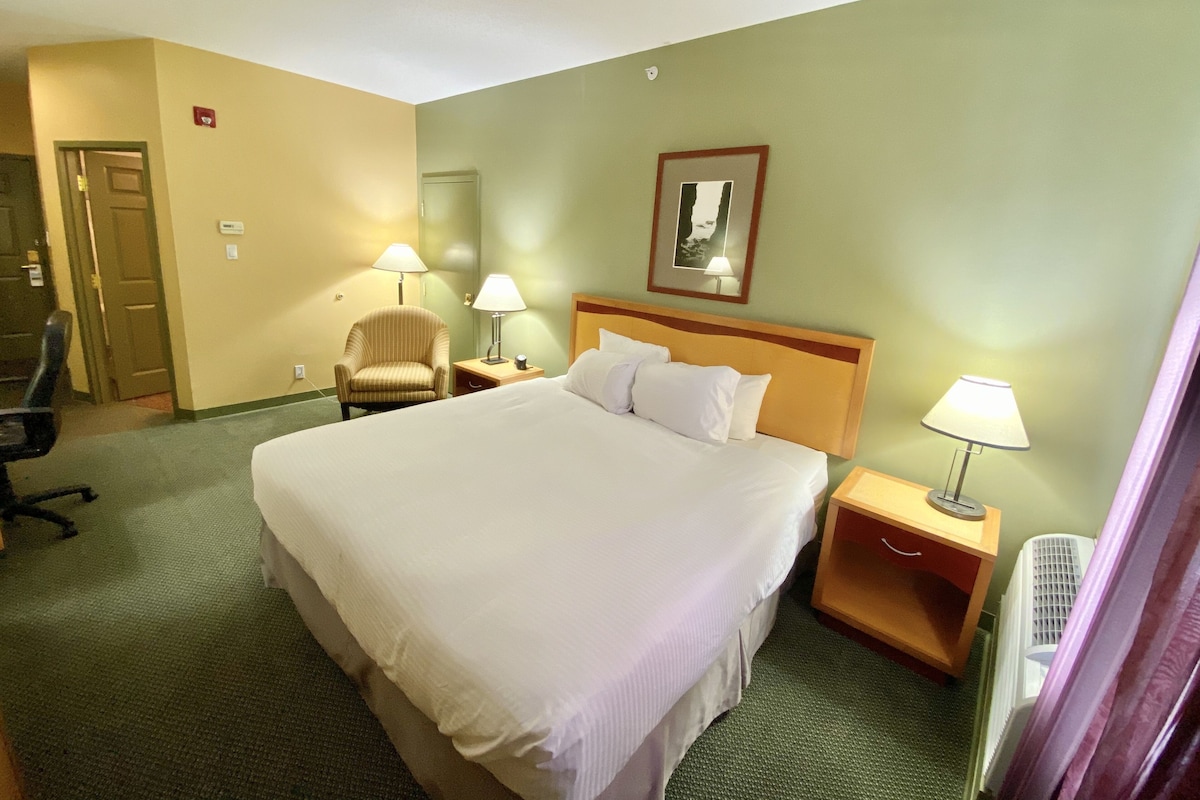 A hotel room with a large bed, two bedside tables with lamps, a chair, and a door.