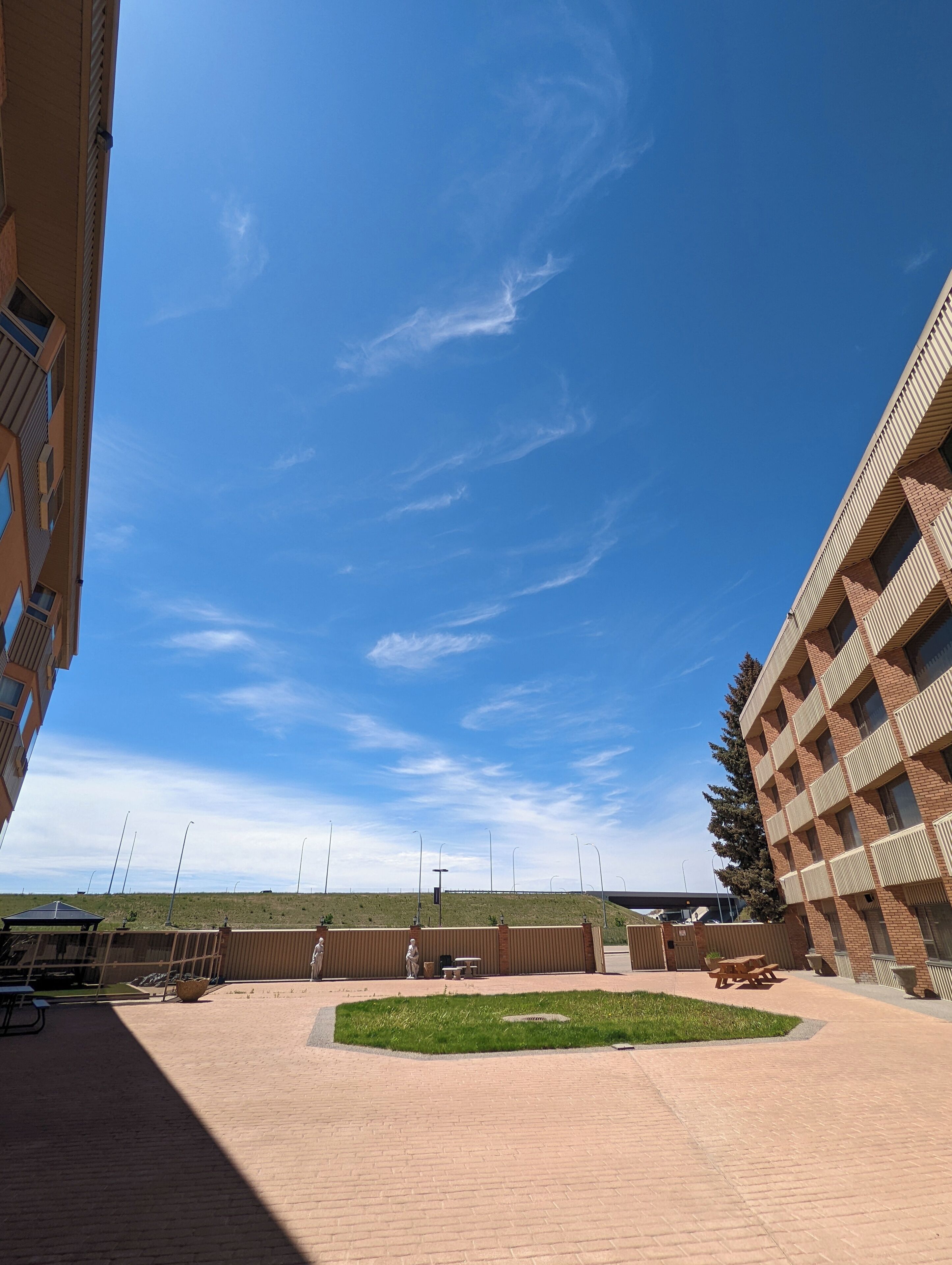 Une cour extérieure, avec un ciel d’un bleu limpide, une pelouse et un bâtiment en briques doté d’un design géométrique original.