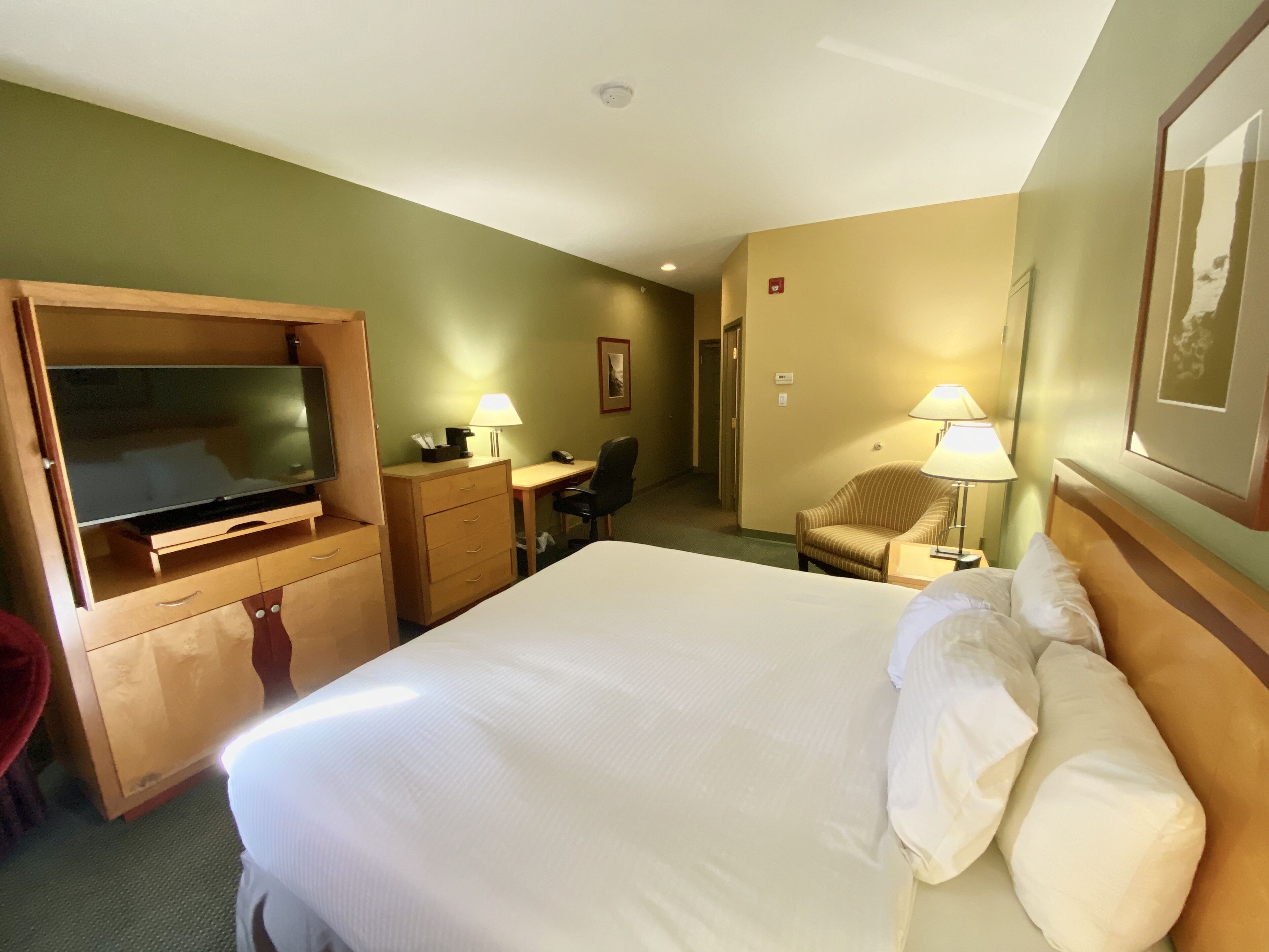 Una habitación de hotel con cama, escritorio, silla, televisor y lámpara.
