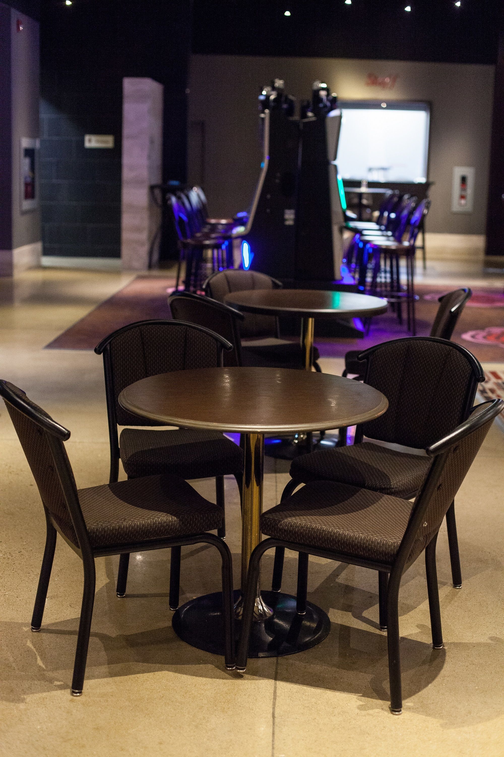 A restaurant with round tables and dark chairs, a counter with a menu board, and a projection screen in the background.
