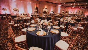 A banquet hall with round tables set for a formal event, featuring dark tablecloths, white chairs, and floral centerpieces.