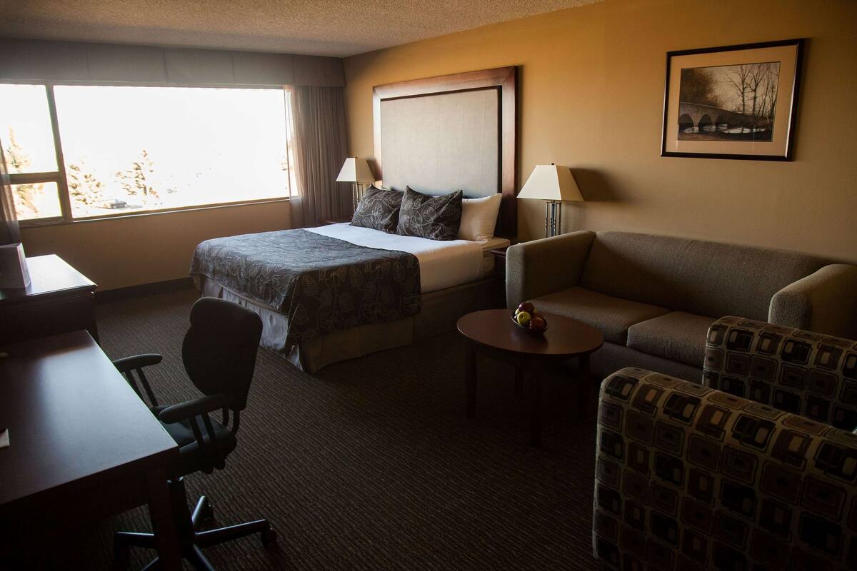 A hotel room with a bed, two bedside tables with lamps, a sofa, a small table with fruit, and a desk.