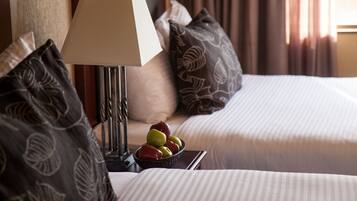 Habitación de hotel con dos camas, una mesita de noche con lámpara, un frutero y almohadas estampadas.