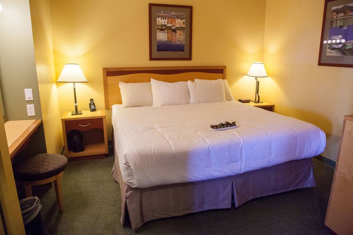 A hotel room with a large bed, two bedside tables with lamps, a chair, and a small table with a phone.