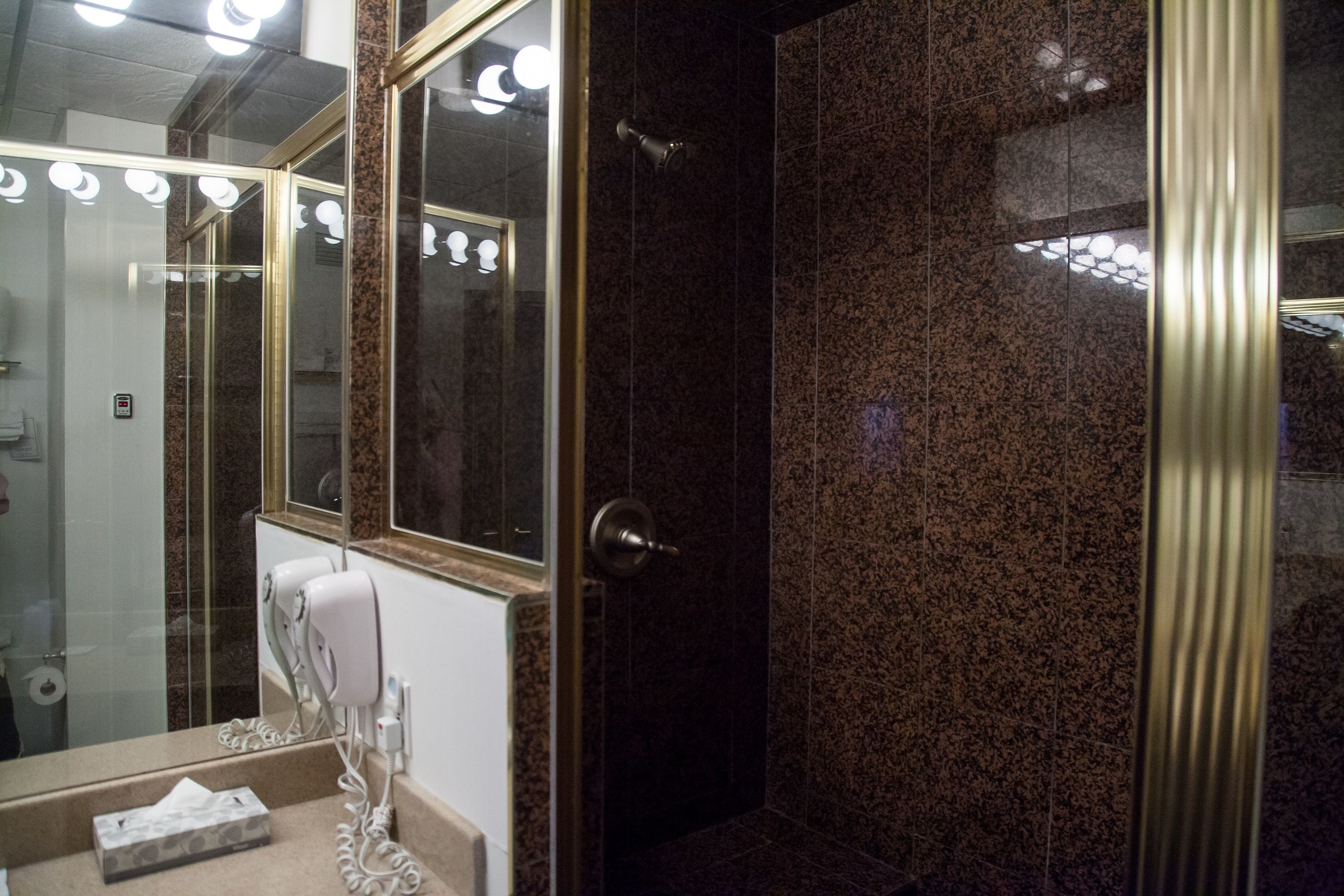 A bathroom with a marble wall, a glass shower enclosure, and a vanity with a towel and a hairdryer.