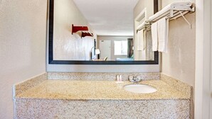 A bathroom with a granite countertop, a white sink, and a large mirror.