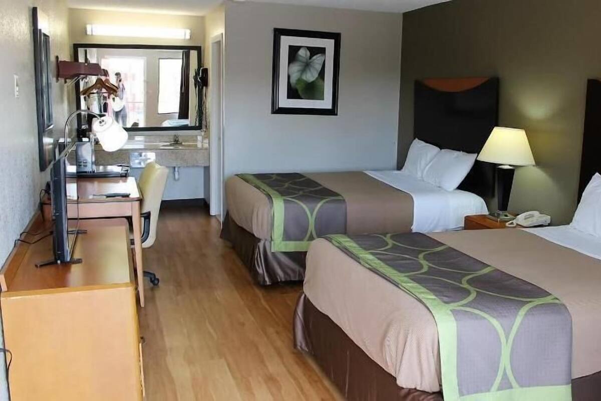 A hotel room with two beds, a desk with a chair, a mirror, a framed picture on the wall, and a nightstand with a lamp.